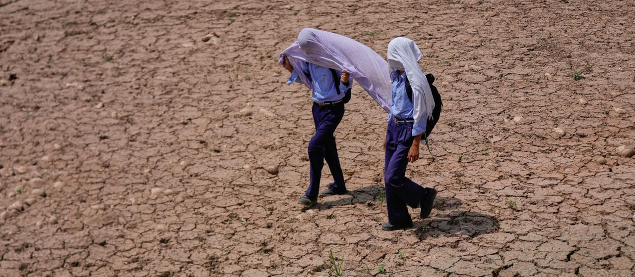 Kinder in Indien auf dem Weg zur Schule versuchen sich mit Tüchern vor Hitze und Sonne zu schützen.