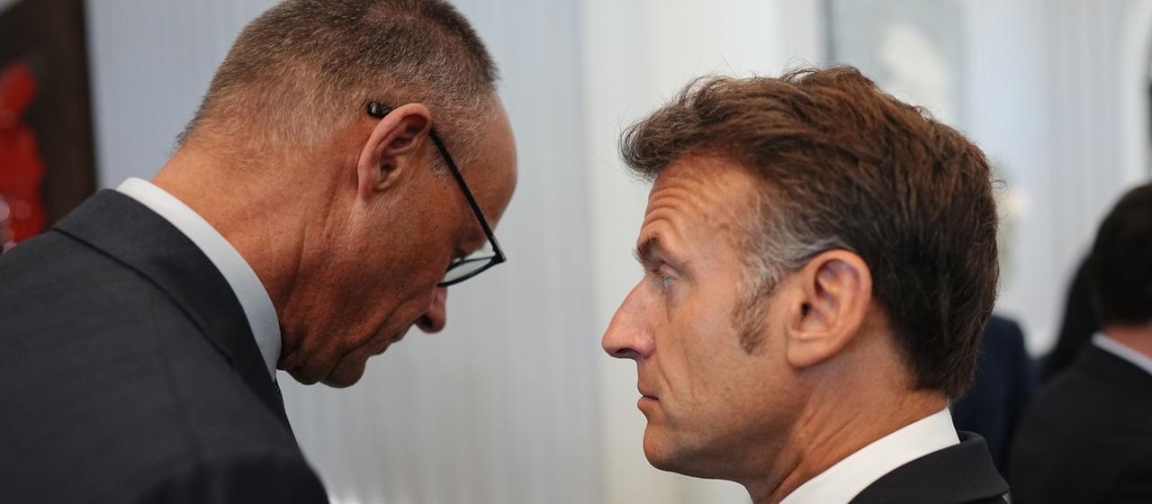 Emmanuel Macron mit hochgezogener Augenbraue, von ihm abgewandt Friedrich Merz