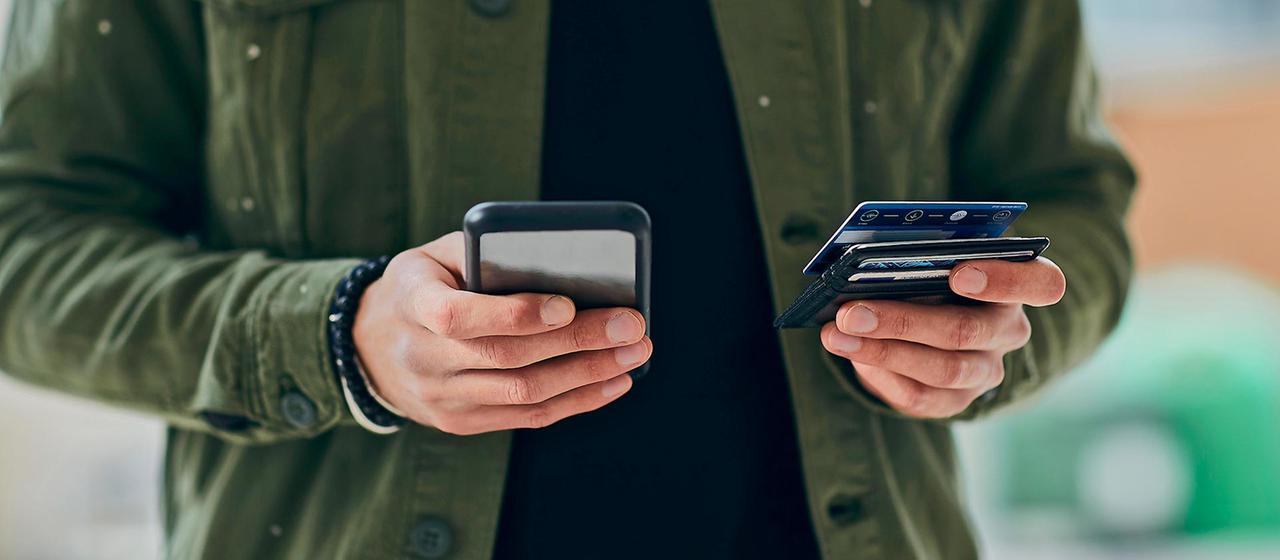 Eine Person hält ein Smartphone und eine Kreditkarte in Händen.