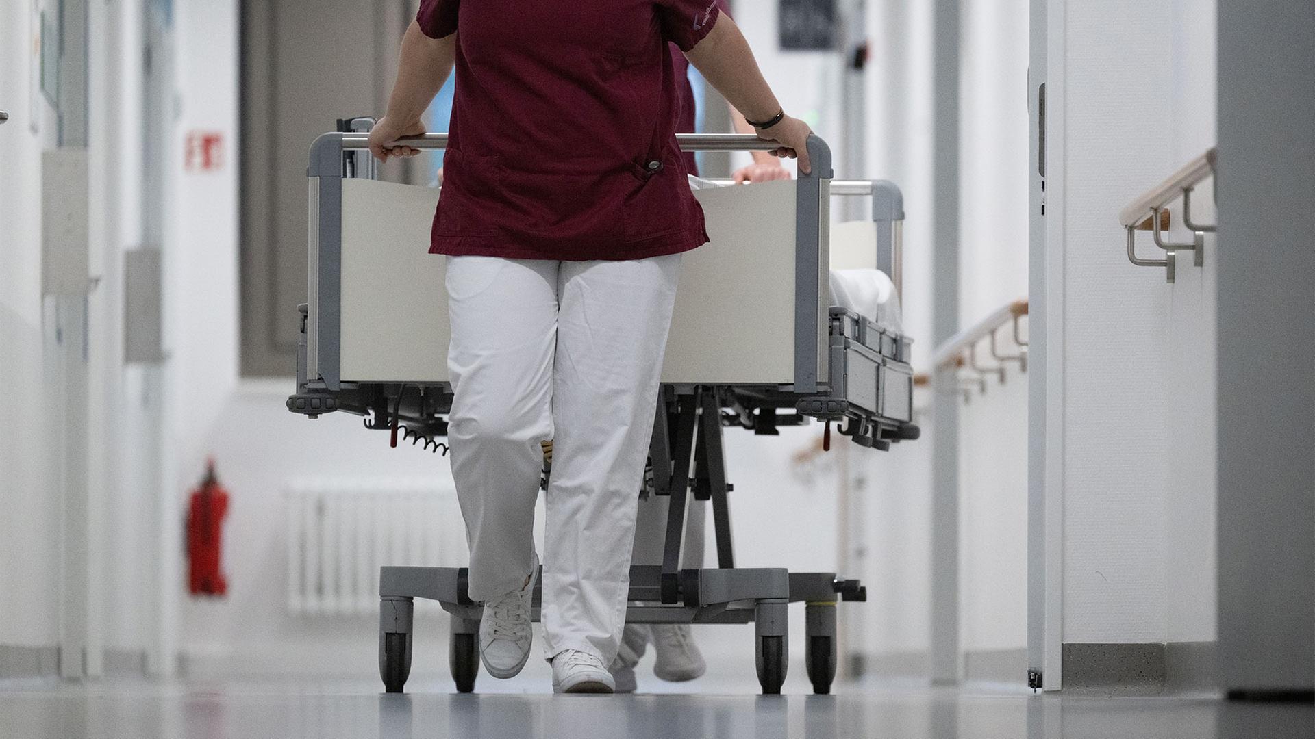 Pflegekräfte schieben ein Krankenbett auf einer Station eines Krankenhauses. | picture alliance/dpa