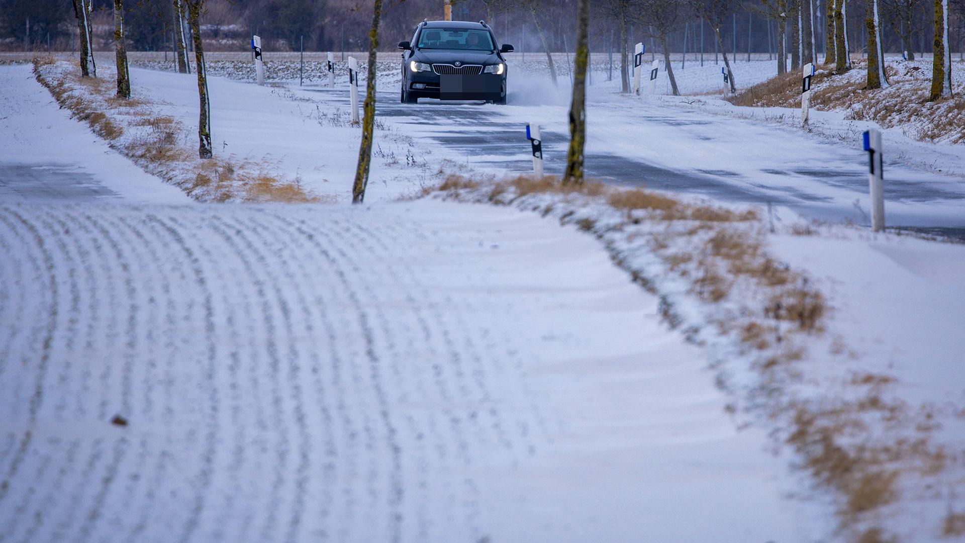 Ein Auto fährt in Mecklenburg-Vorpommern über eine teilweise mit Schnee bedeckte Straße. | Jens Büttner/dpa