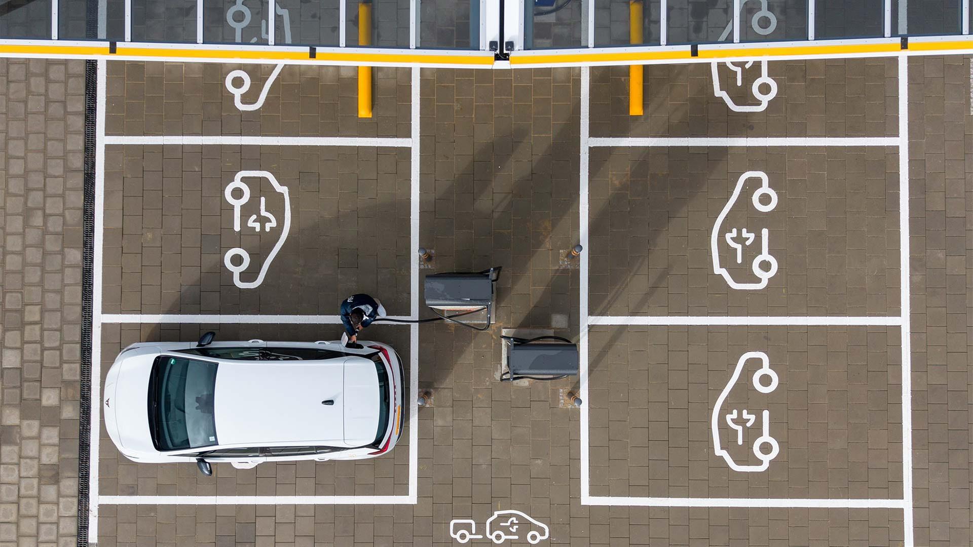 Drohnenaufnahme von einem Mann der sein E-Auto in einem Ladepark auflädt. | picture alliance/dpa