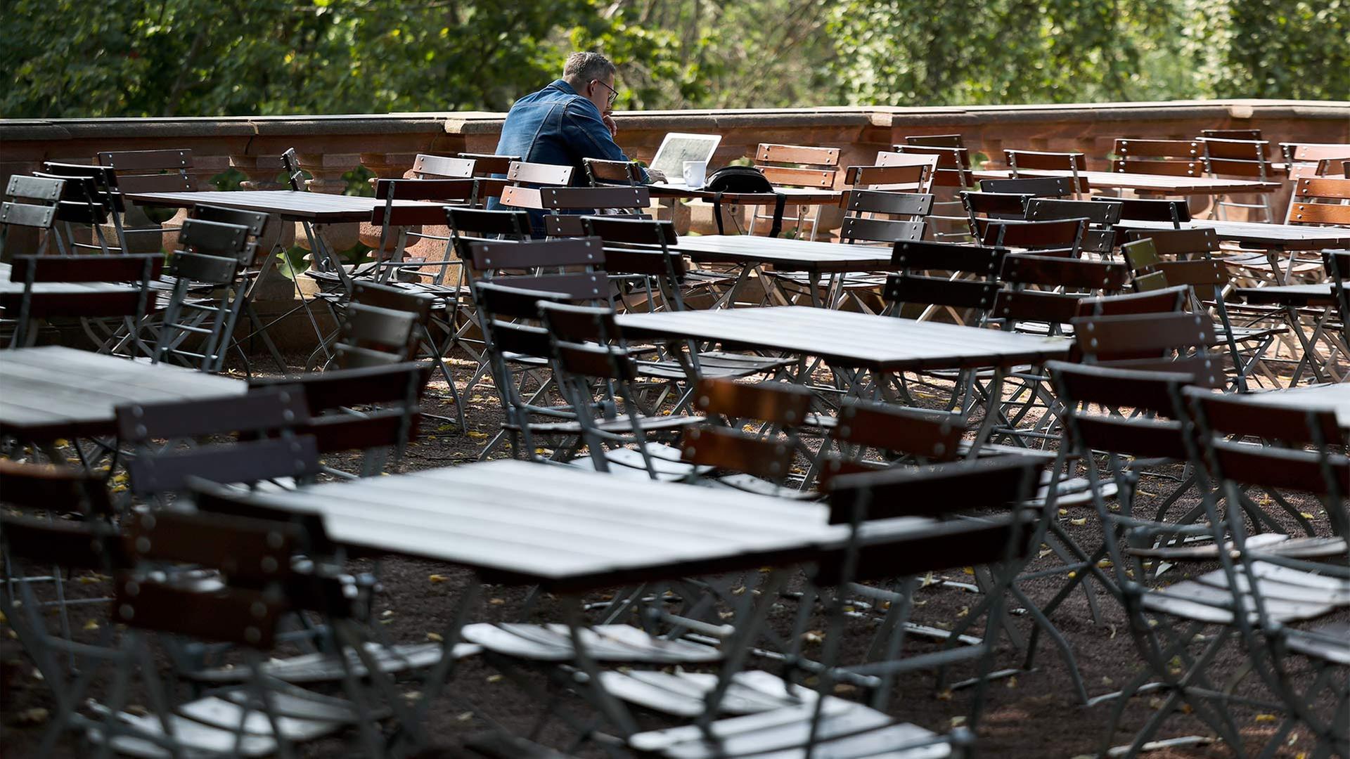 Ein Mann sitzt in einem ansonsten leeren Biergarten. | picture alliance/dpa