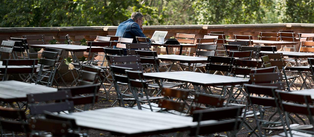 Ein Mann sitzt in einem ansonsten leeren Biergarten.