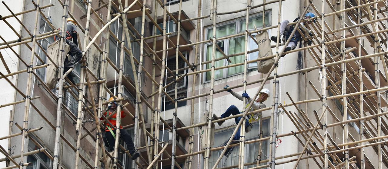 Arbeiter errichten Bambusgerüste für die Instandhaltung von Außenwänden.