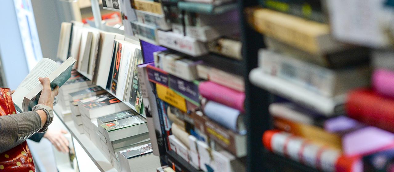 Eine Frau blättert vor einem Regal in einem Buch.