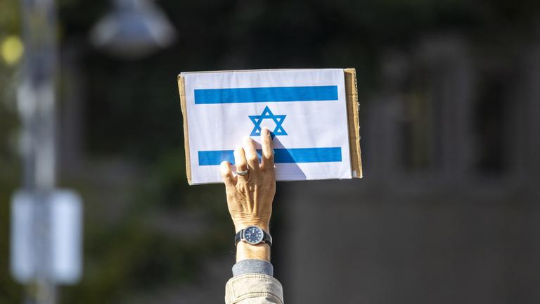Ein Teilnehmer einer Kundgebung hält ein Schild mit der israelischen Flagge in die Höhe. 
