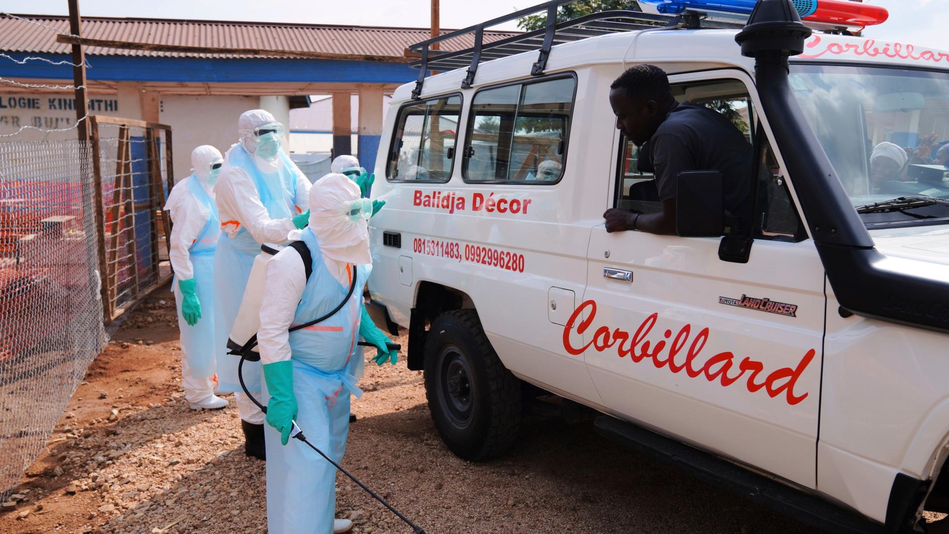Medizinisches Personal desinfiziert einen Krankenwagen. | Dirole Lotsima Dieudonne/AP/dpa