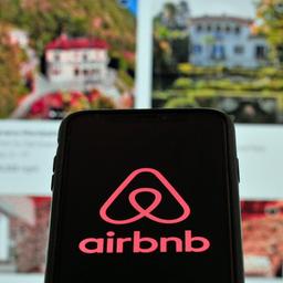 Airbnb-Logo auf einem Smartphone und im Hintergund eine Website mit Mietimmobilien.