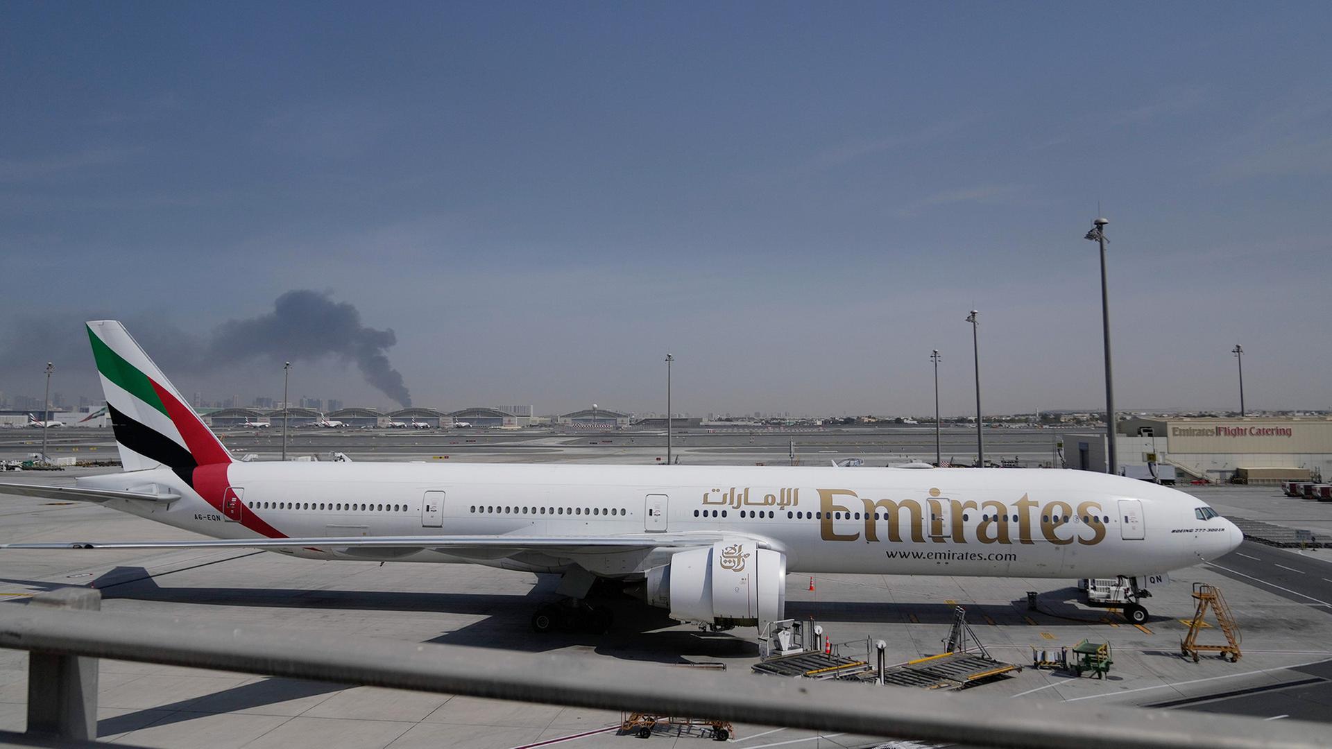 Ein Flugzeug steht auf dem Rollfeld des Flughafens Dubai, wÃ¤hrend im Hintergrund Rauch aufsteigt. | AP