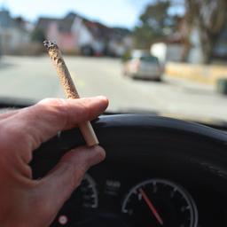 Ein Mann sitzt mit einem Joint zwischen den Fingern am Steuer eines Autos.
