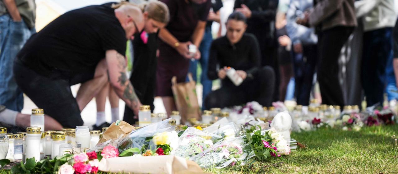 Mehrere Menschen legen an einer Wiesen Blumen nieder