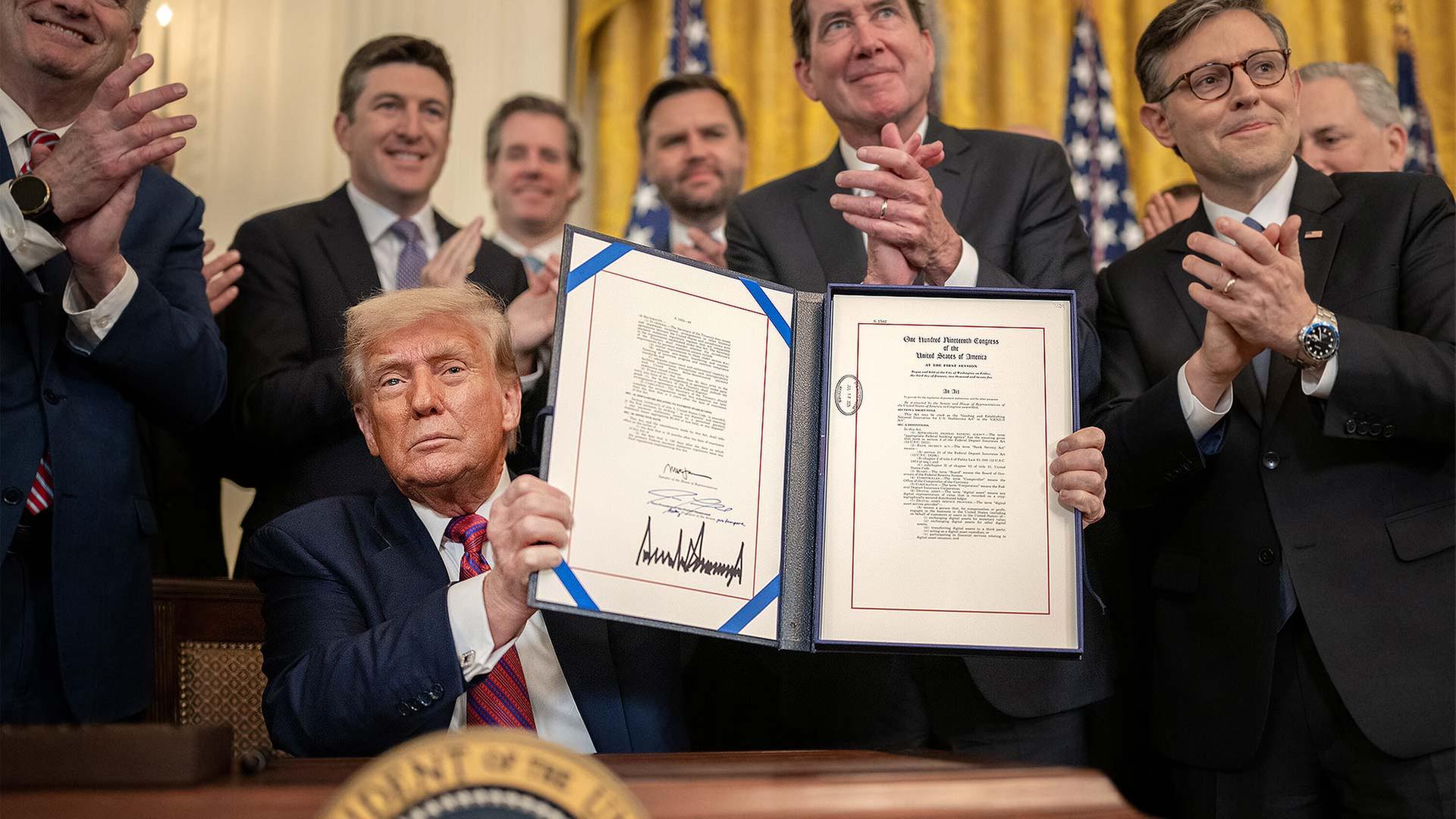 Donald Trump hält das von ihm unterschriebene Dekret zum Genius Act hoch. | picture alliance / ZUMAPRESS.com