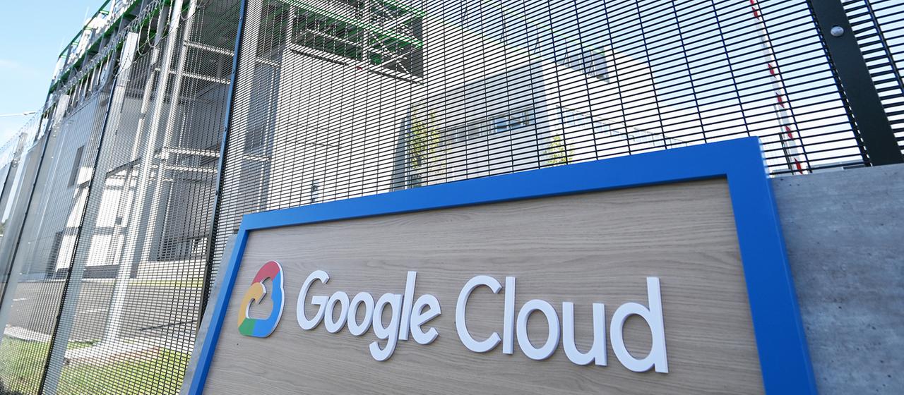 Ein Schild mit der Aufschrift "Google Cloud" ist vor einem mit hohen Stacheldraht gesicherten Rechenzentrum zu sehen.