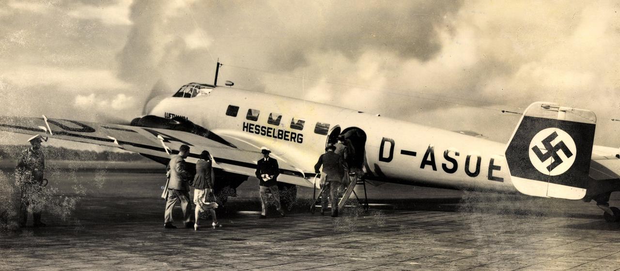 Menschen besteigen ein historisches Flugzeug das auf einem Rollfeld steht.