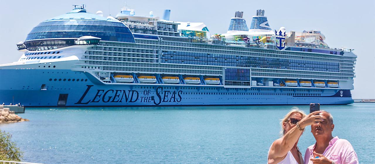 Touristen machen ein Selfie mit einem Kreuzfahrtschiff im Hintergrund.