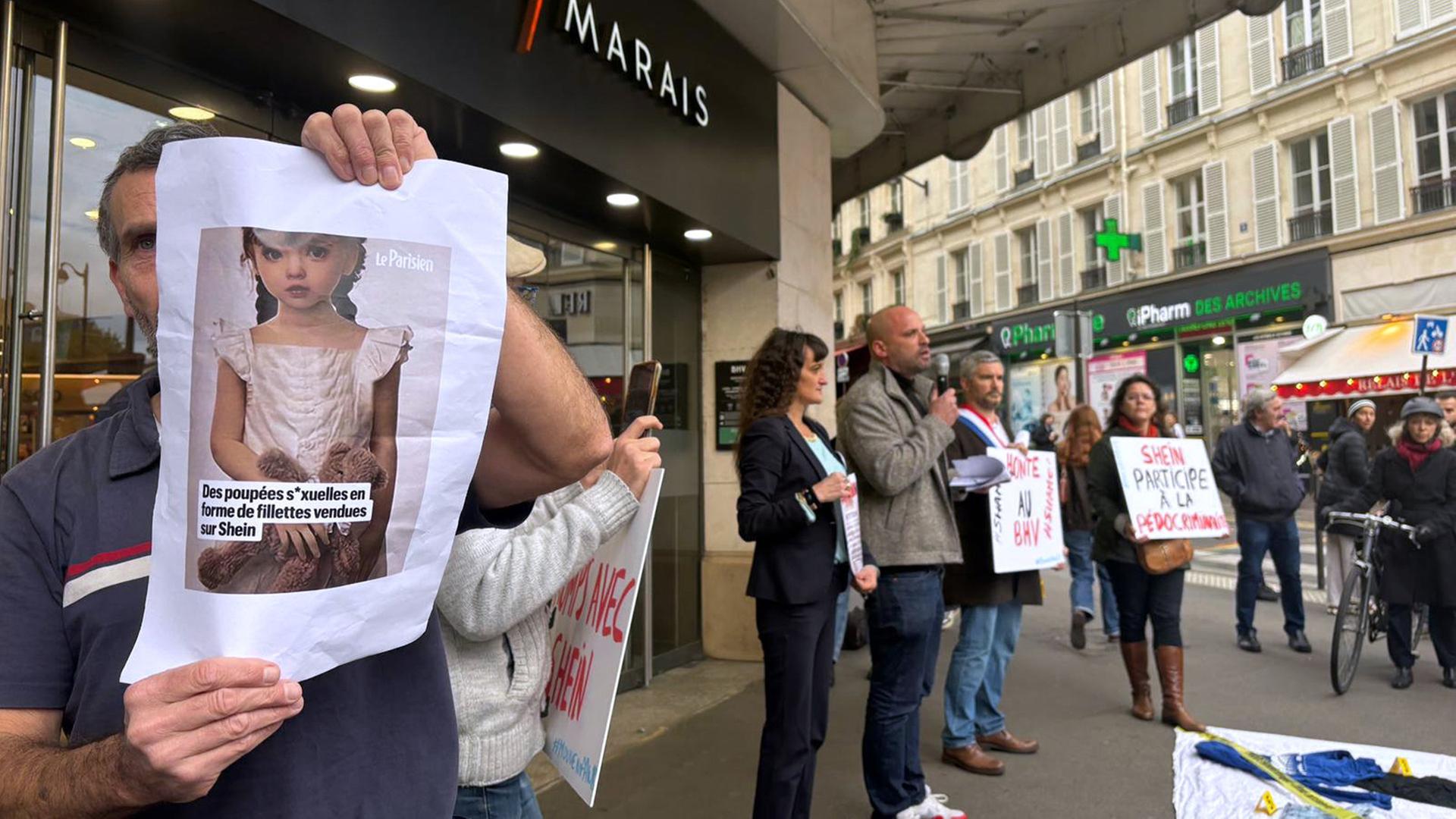 Ein Demonstrant hält ein Bild einer kindlichen Sexpuppe vor dem Kaufhaus BHV Marais in Paris. | AP