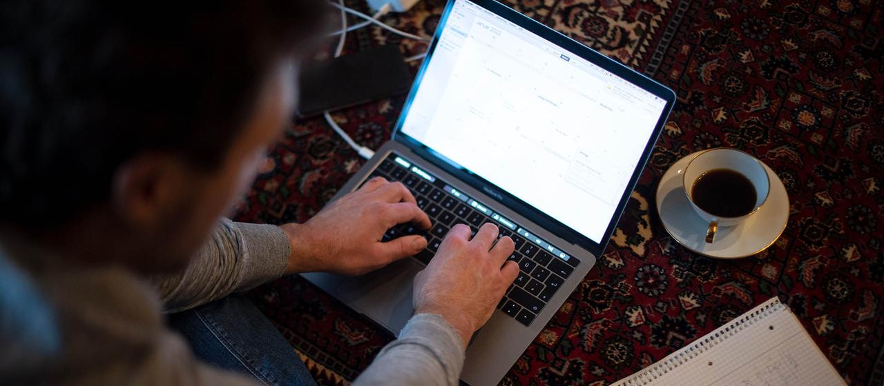 Ein Mann sitzt im Homeofficean seinem Laptop auf einem Teppich.