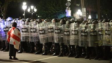 Eine Person, die in eine Georgien-Flagge gehüllt ist, steht einem Polizeiaufgebot in Tiflis gegenüber.