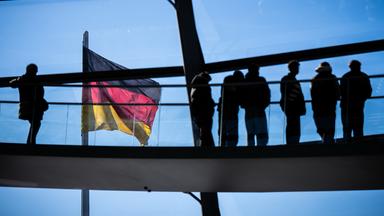  Besucher gehen vor der Deutschlandflagge in der Kuppel im Bundestag. 