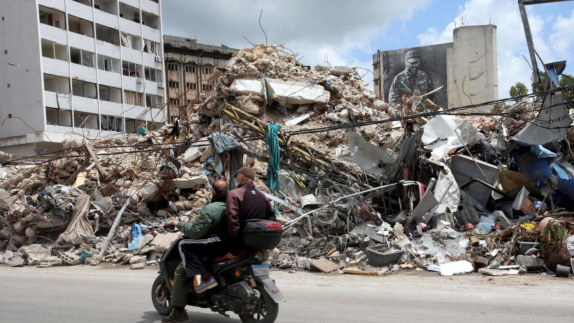Menschen fahren auf einem Motorroller an zerstörten Gebäuden im Süden Libanons vorbei. | AFP