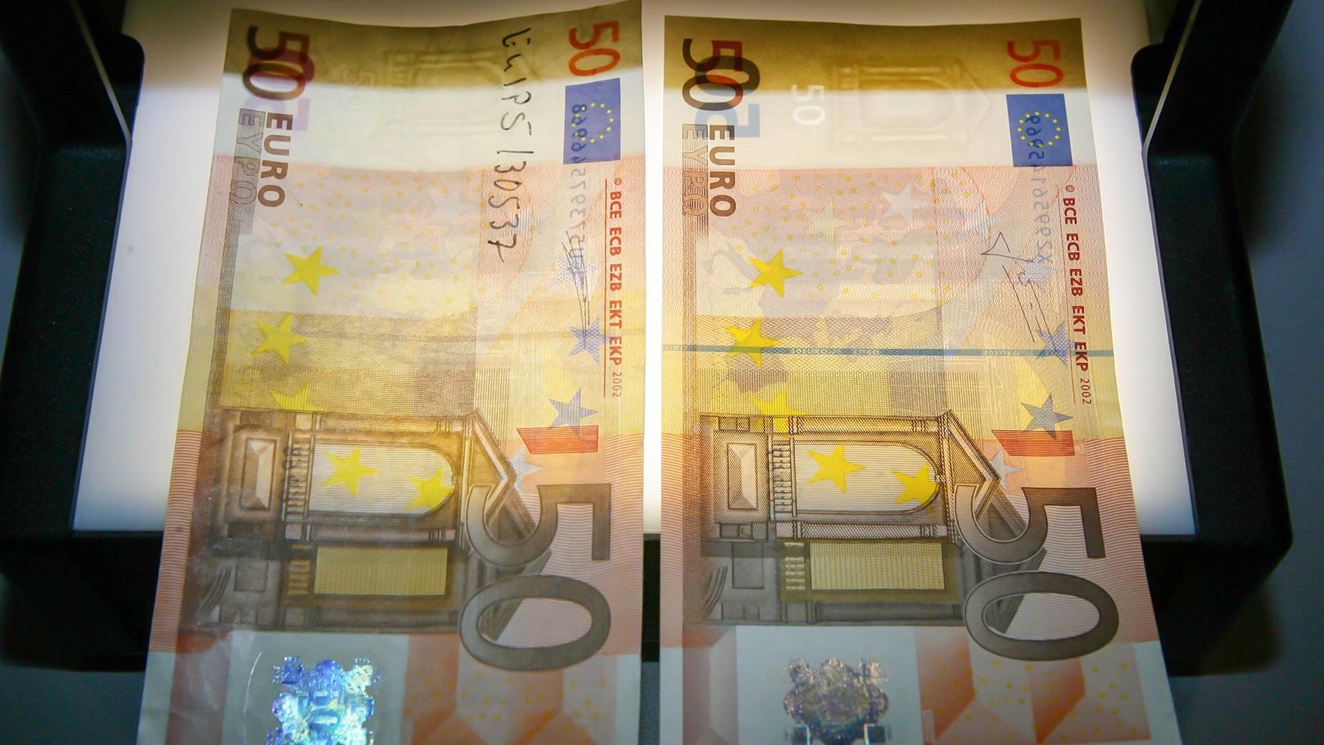 Ein falscher und ein echter F�nfziger liegen auf einem Leuchtger�t (Archivbild). | dpa
