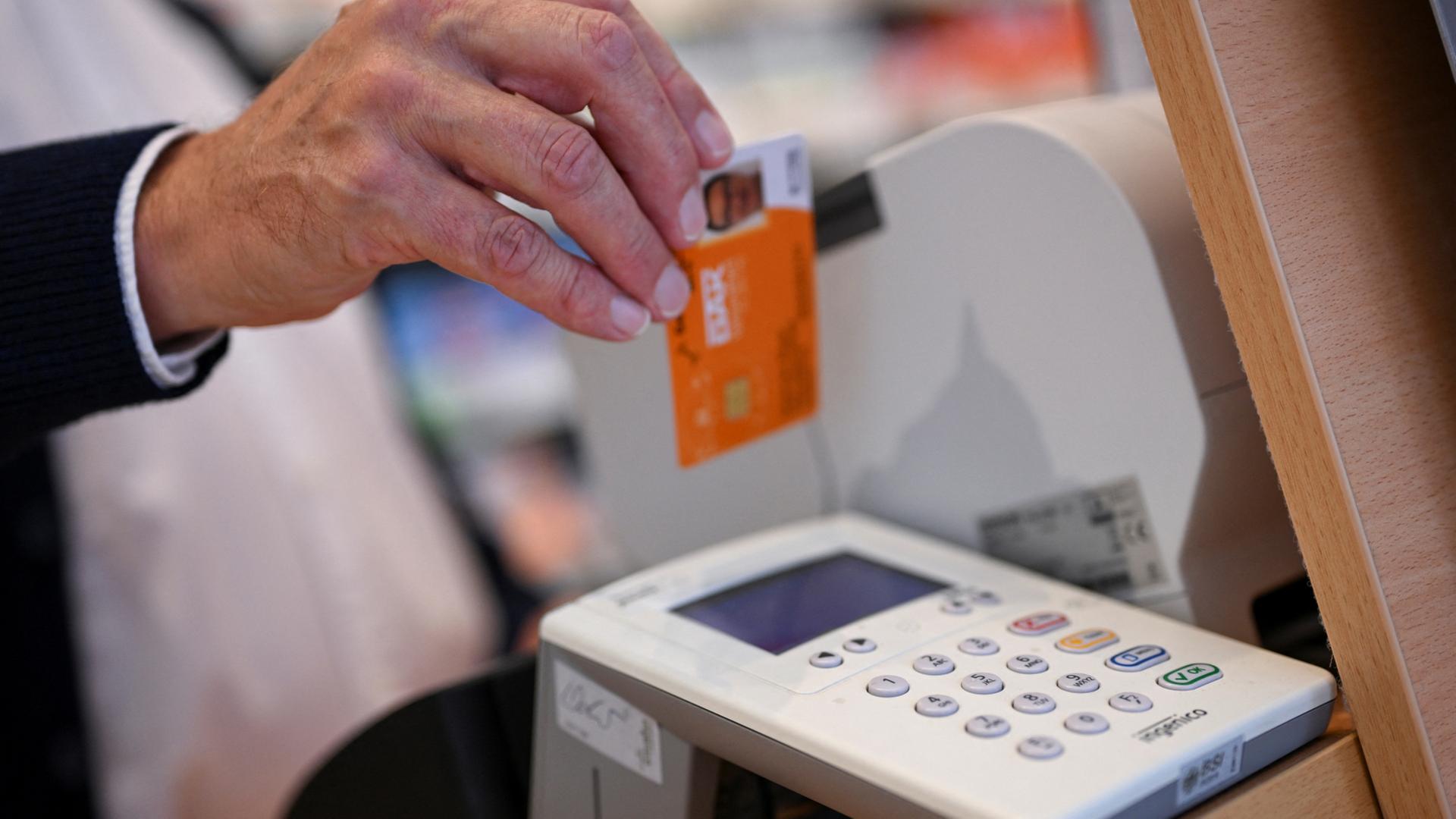 Eine Person steckt die Gesundheitskarte eines Patienten in ein Kartenlesegerät in einer Apotheke. | dpa