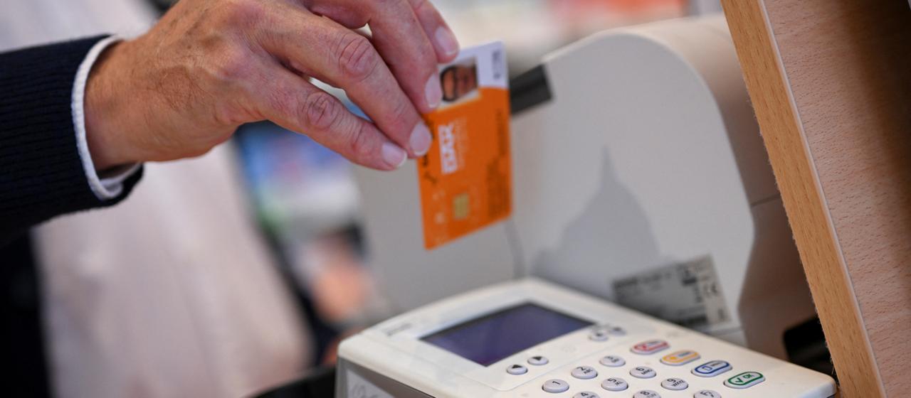 Eine Person steckt die Gesundheitskarte eines Patienten in ein Kartenlesegerät in einer Apotheke.