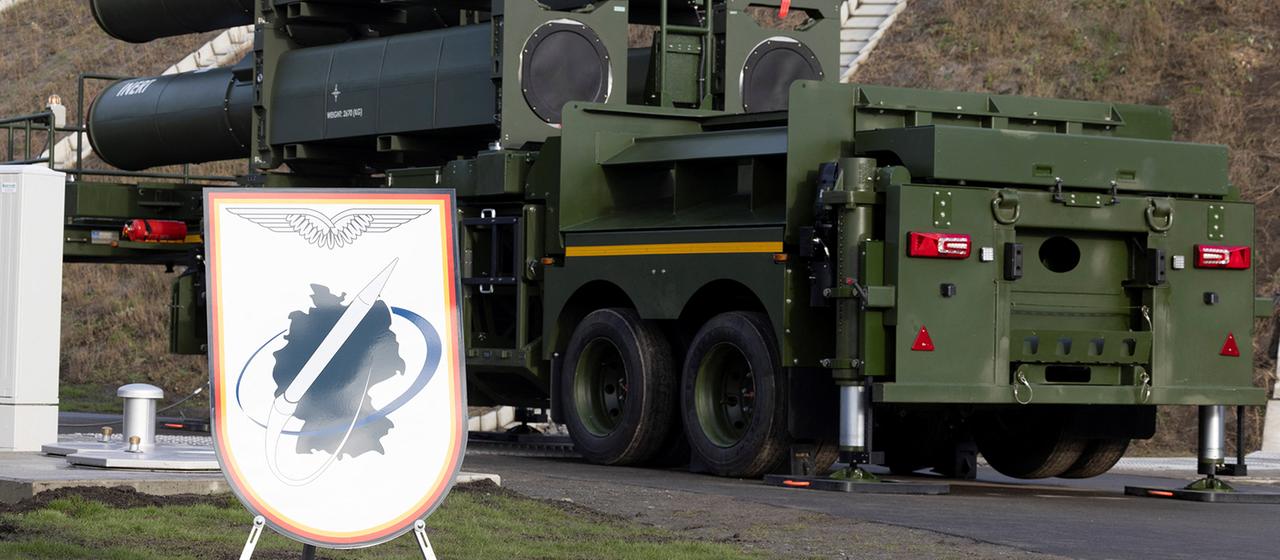 Ein Schild, das die Bundesrepublik Deutschland zeigt, steht neben militärischem Gerät.