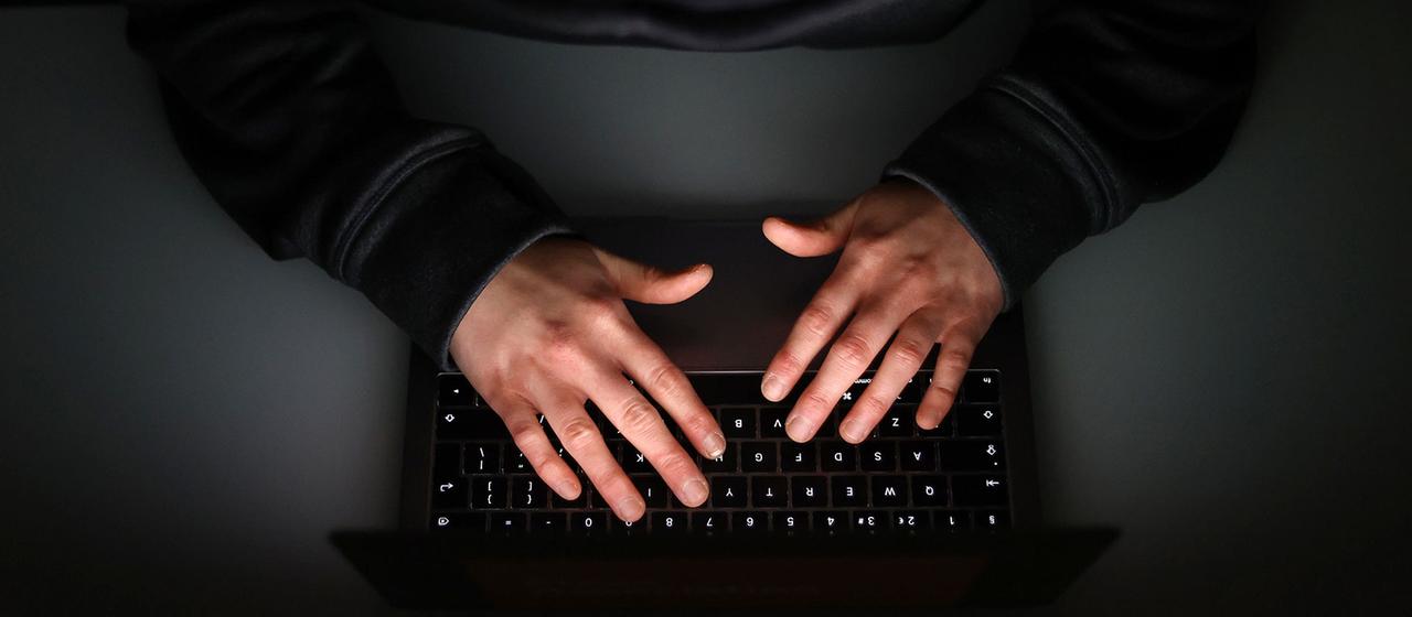 Hände tippen auf eine beleuchteten Tastatur.