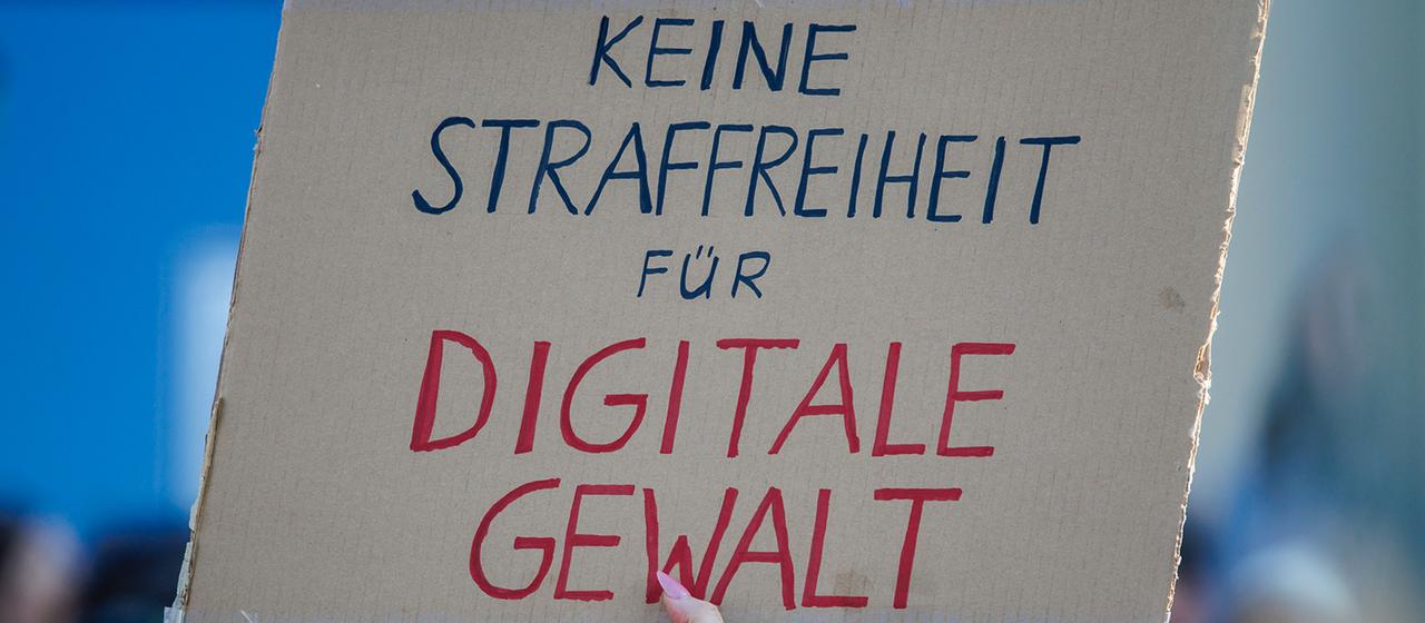 Bei einer Demonstration wird ein Pappschild mit der Aufschrift "Keine Strafffreiheit für digitale Gewalt" hoch gehalten.