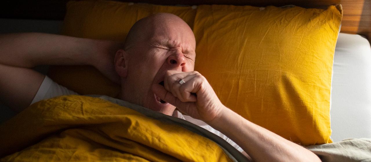 Ein Mann liegt gähnend im Bett.