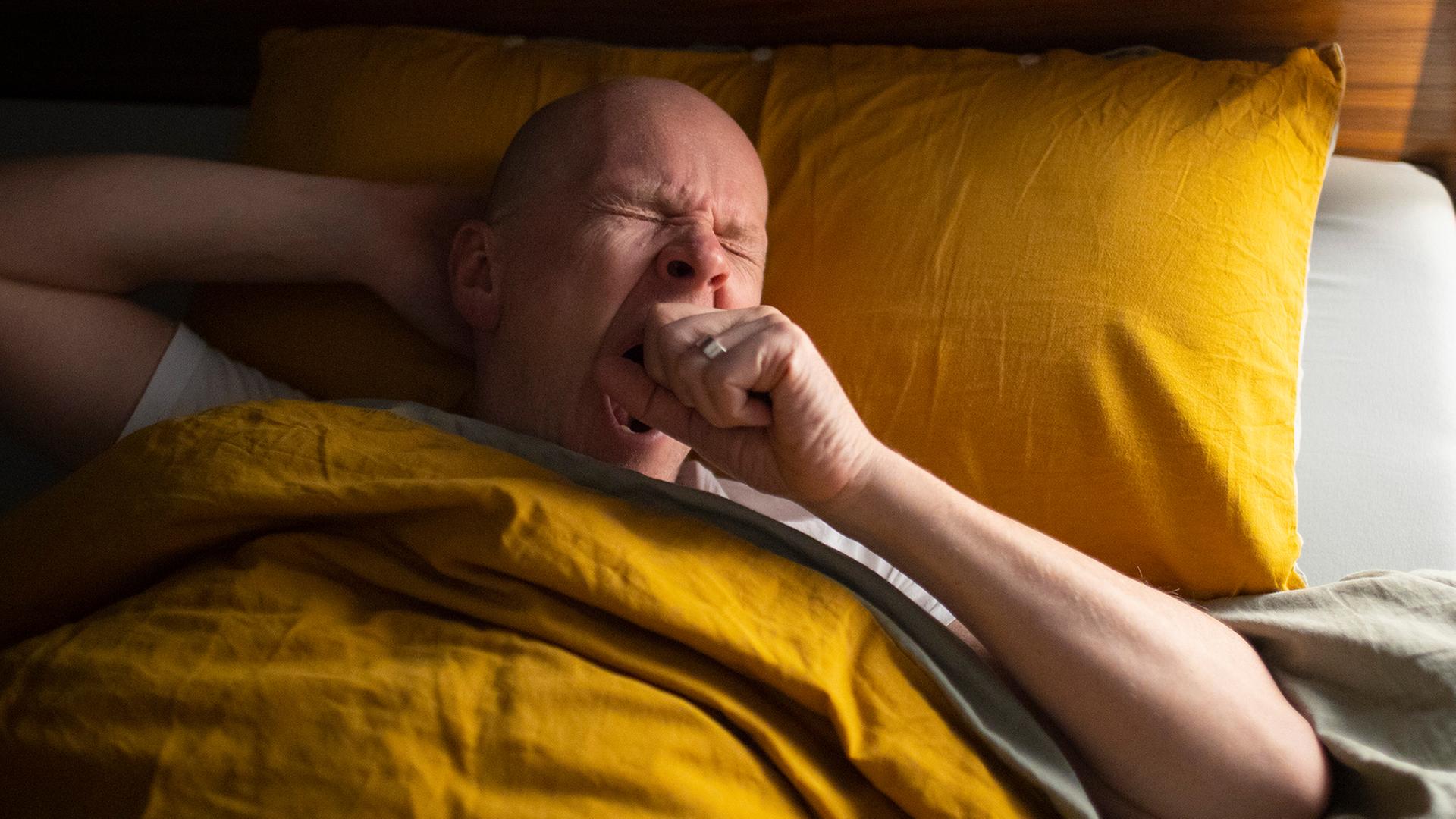 Ein Mann liegt gähnend im Bett. | picture alliance / photothek