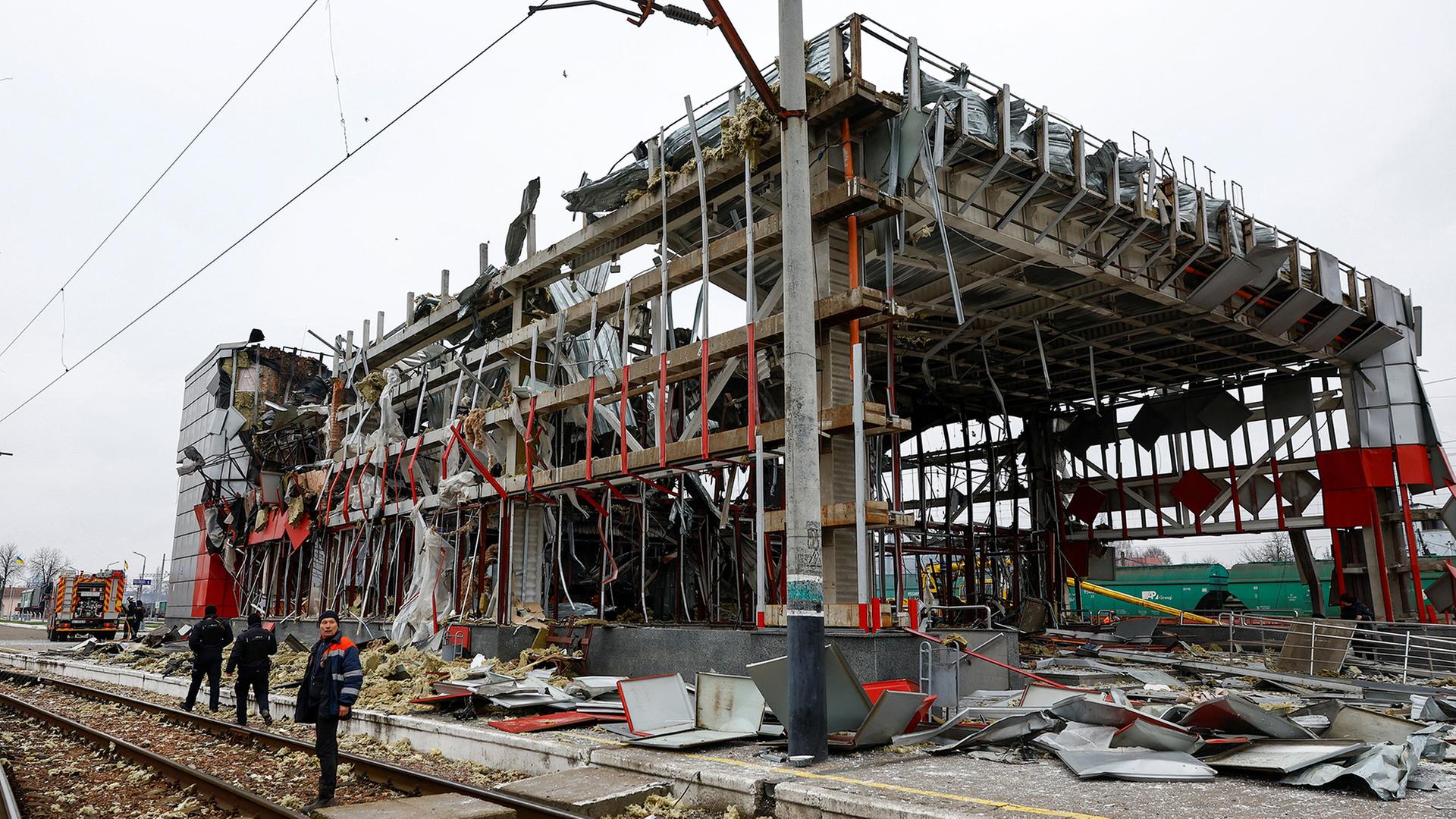 Bahnmitarbeiter stehen vor einem zerstörten Bahnhofsgebäude ein Fastiw. | REUTERS