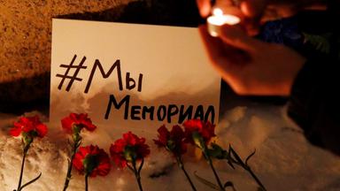 Blumen liegen vor einem Plakat mit der Aufschrift "#WirSindMemorial" in Sankt Petersburg, Russland