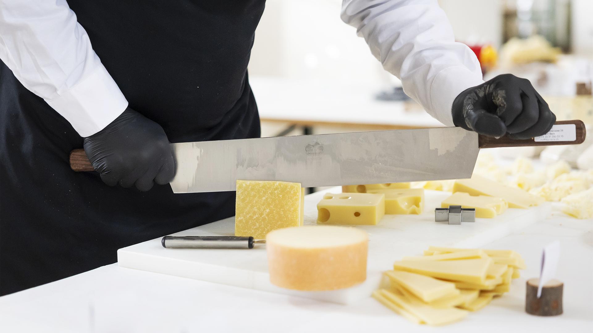 Ein Mann schneidet Käse mit einem großen Käsemesser.