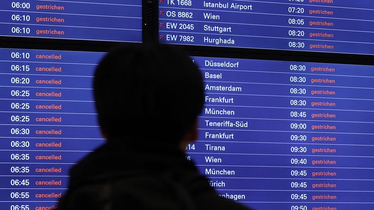 Ein Mann schaut am Flughafen Hamburg auf eine Anzeigentafel, auf der zahlreiche gestrichene Flüge angezeigt werden. 