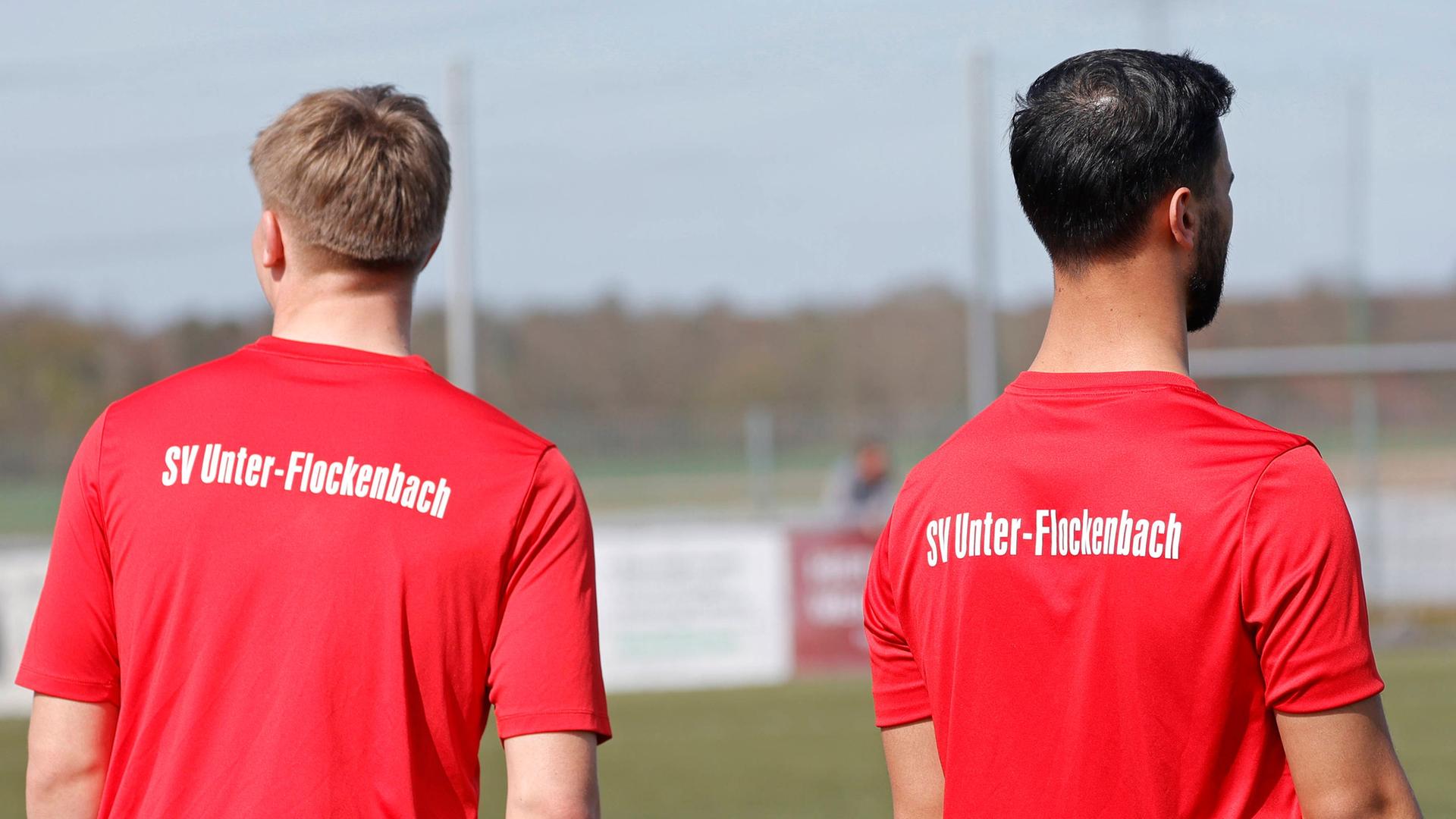 Die Rücken von zwei Spielern sind zu sehen. Auf ihren T-Shirts steht 