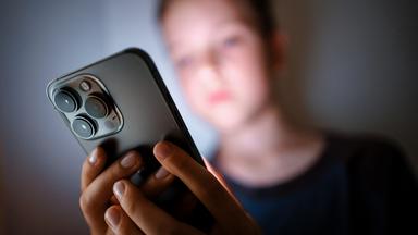 Ein Kind schaut im Dunkeln auf das Display eines Smartphones