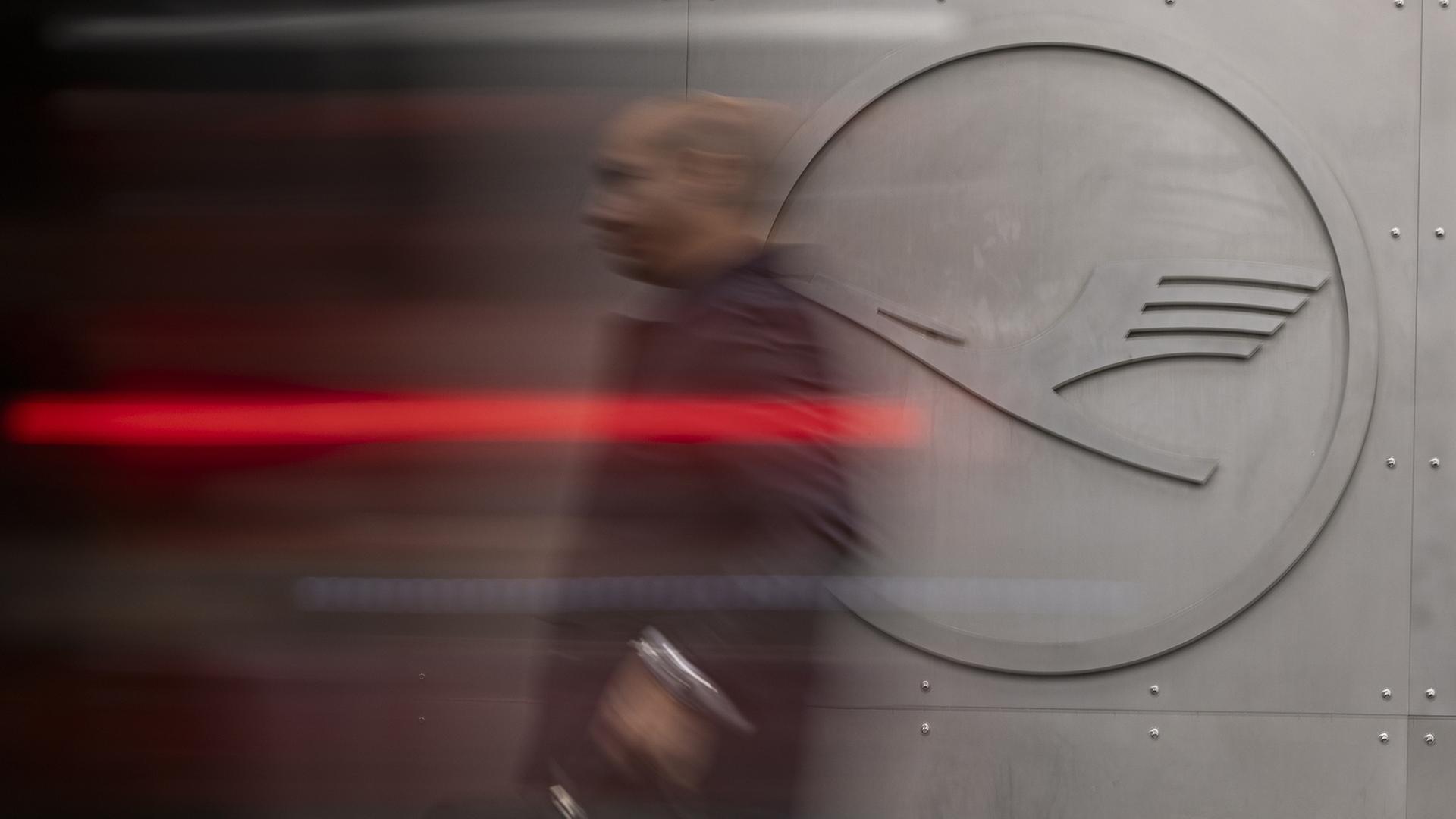 Ein Mann geht an einem Lufthansa-Logo vorbei. | dpa