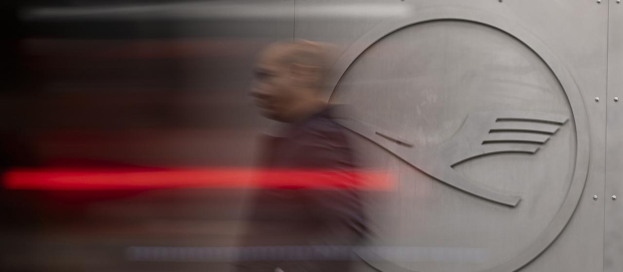 Ein Mann geht an einem Lufthansa-Logo vorbei.