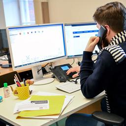 Mann sitzt vor Computer-Bildschirm und telefoniert.