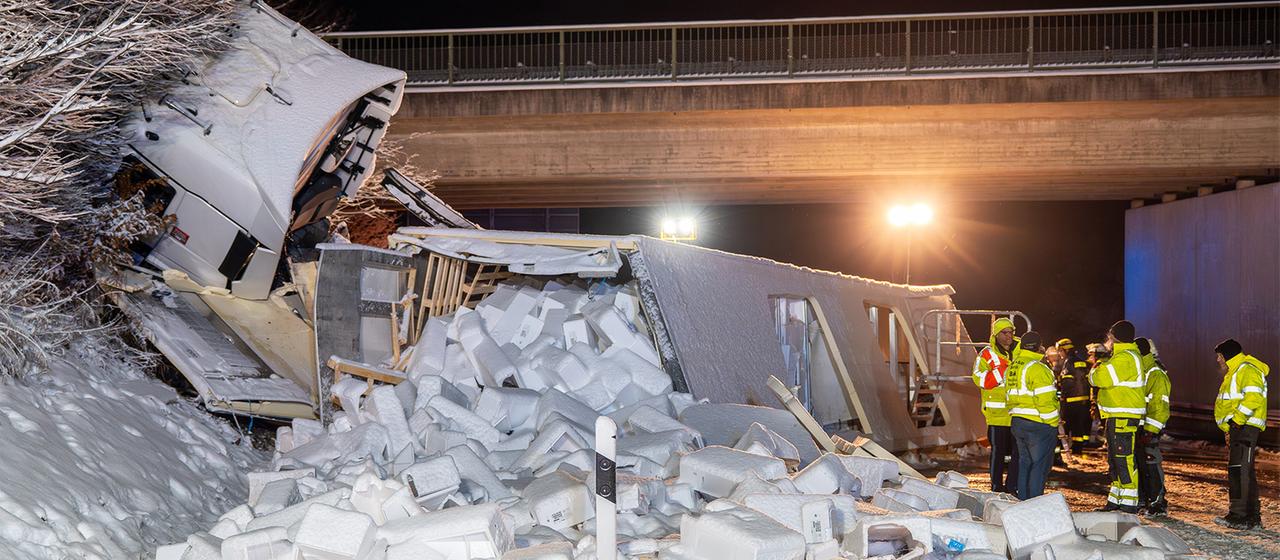 Die Ladung eines Lastwagens liegt nach einem Unfall neben der Fahrbahn im Schnee.