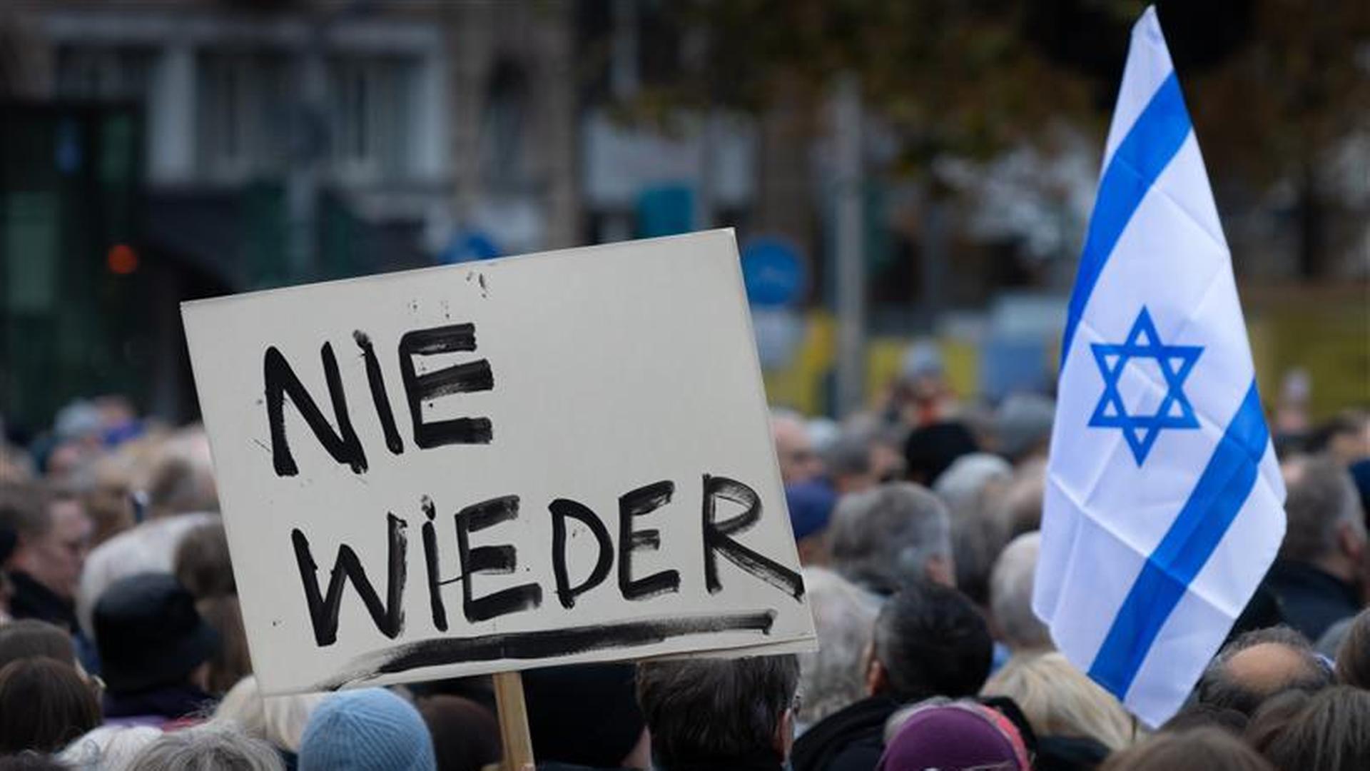 Demonstranten-Köpfe von hinten, es wird eine Israel-Flagge hochgehalten und ein Schild mit der Aufschrift 