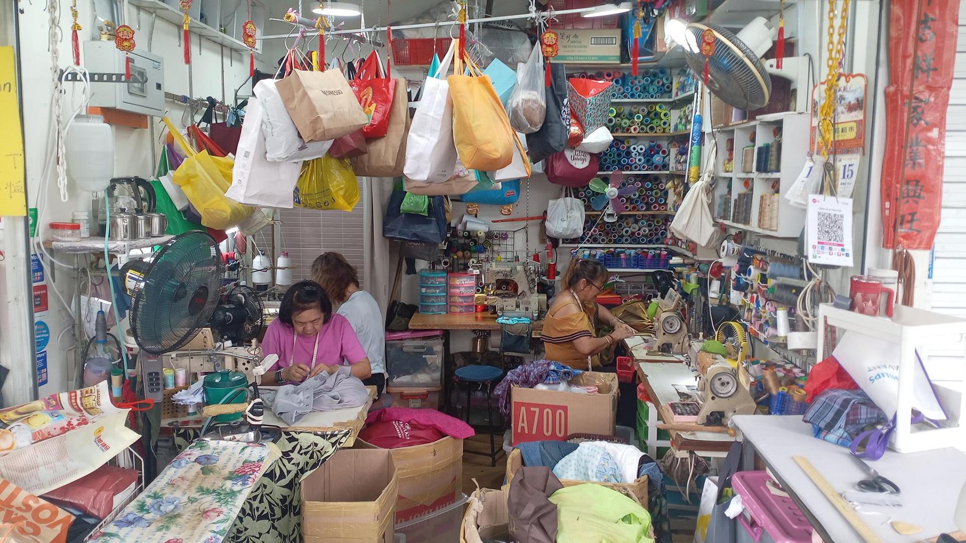 Schneiderinnen sitzen in einem Raum mit vielen Taschen und Nähutensilien. | ARD-Singapur
