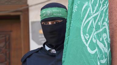 Ein maskiertes Mitglied der Kassam-Brigade steht neben der grünen Flagge der Hamas.