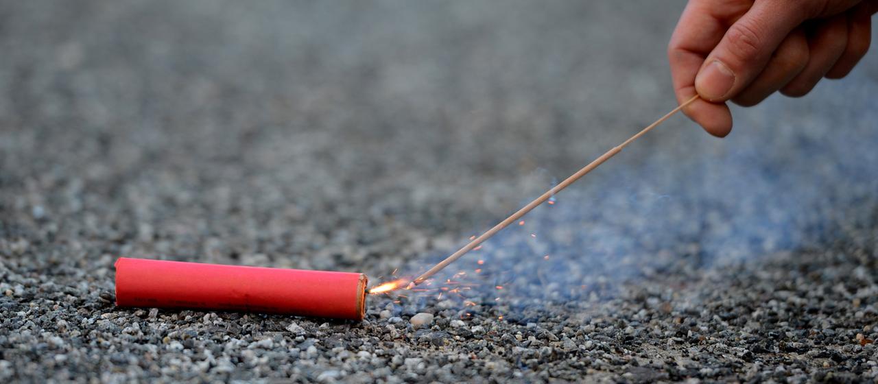 Eine Person zündet einen Böller mit einer Wunderkerze an.