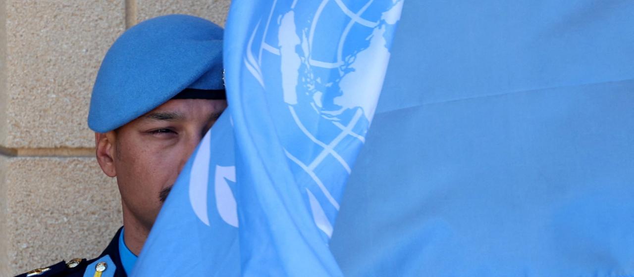 Ein UN Blauhelm-Soldat wird zur Hälfte von einer blauen UN-Flagge verdeckt