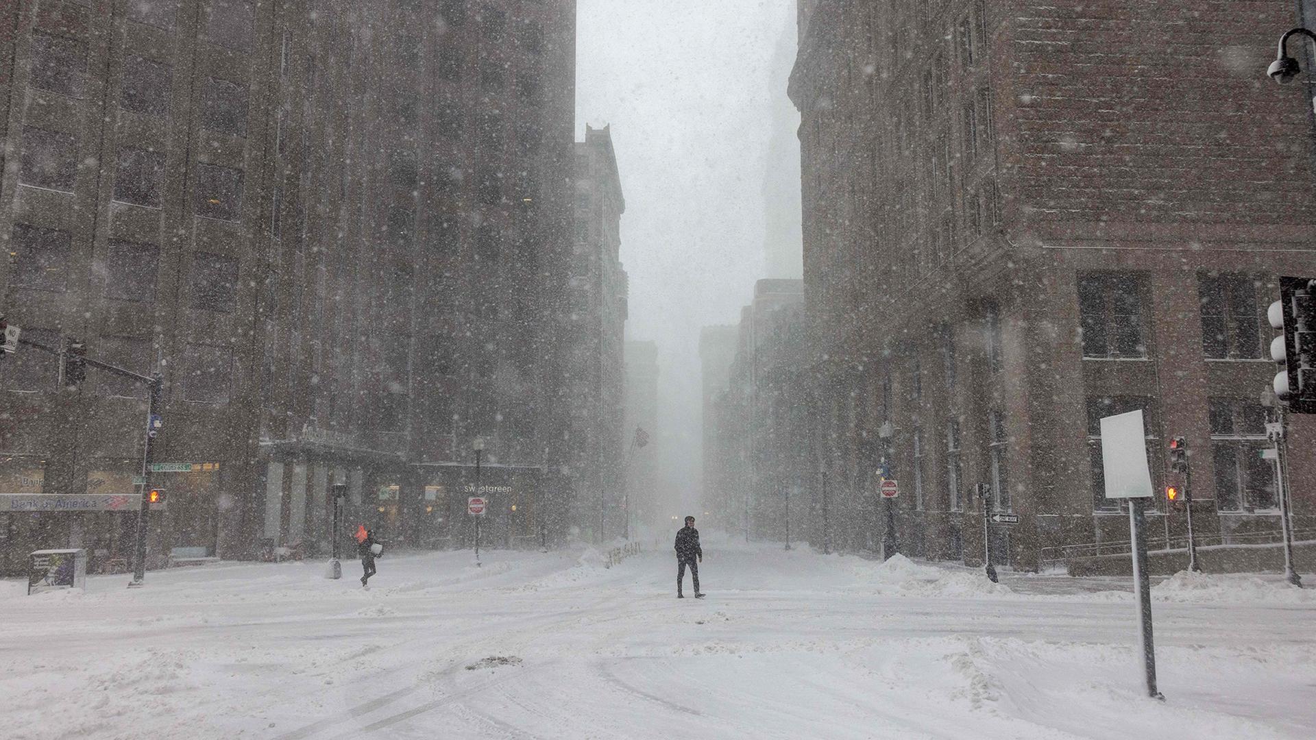 Menschen überqueren bei starkem Wind und heftigem Schneefall eine Straße in Boston (Massachusetts, USA). | Getty Images via AFP