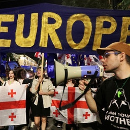 Demonstranten auf der Straße bei Dunkelheit, einer hält ein Megafon in der Hand, auf einem Plakat steht "Yes Europe".